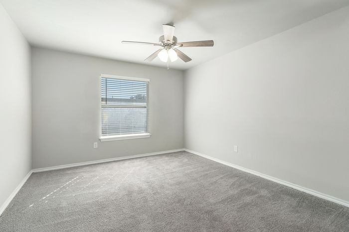 Bright and spacious bedroom with soft carpeting, modern ceiling fan, and ample natural light through a large window.