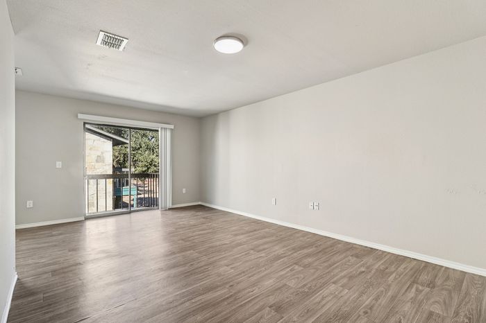 Bright and spacious living room with modern wood flooring and a large sliding glass door opening to a serene outdoor view.