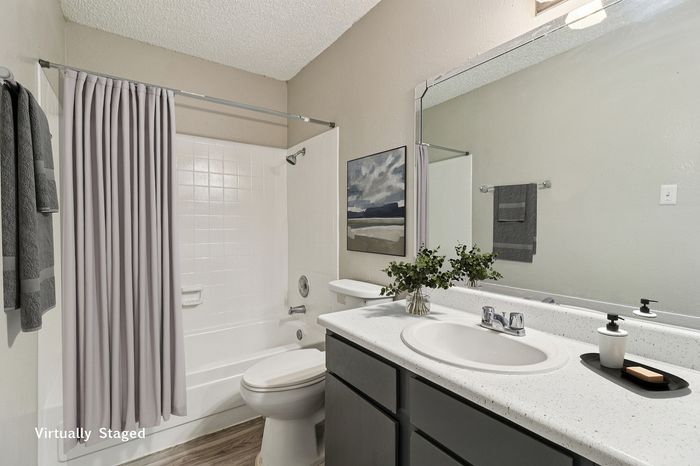 Modern bathroom with elegant decor, featuring a sleek white countertop, lush greenery, and stylish artwork by the tub.