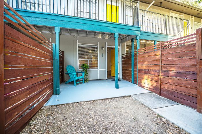Charming patio entrance with vibrant teal accents, a cozy seating area, and rustic wooden fencing.
