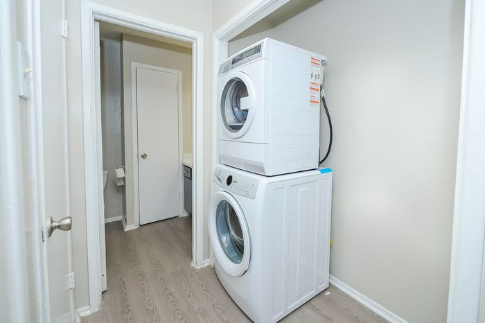 Modern laundry area featuring a sleek stacked washer and dryer, set against a stylish gray wood floor, perfect for convenient apartment living.