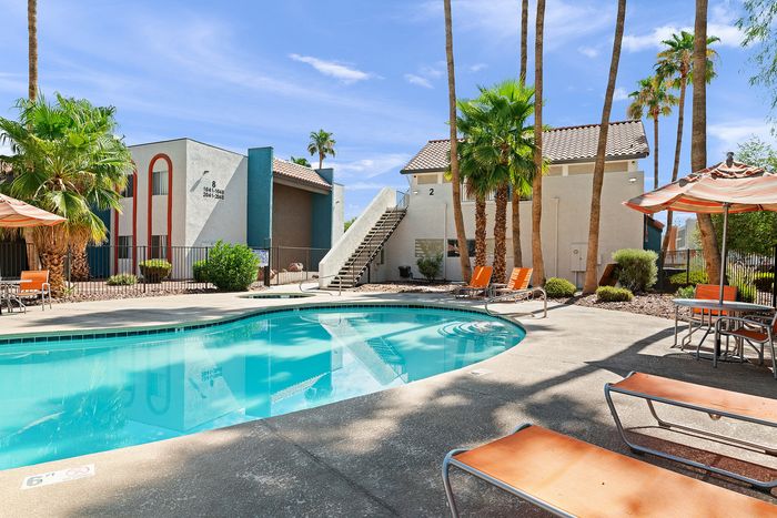 Inviting apartment complex with palm trees and a shimmering swimming pool, offering a relaxing outdoor escape.