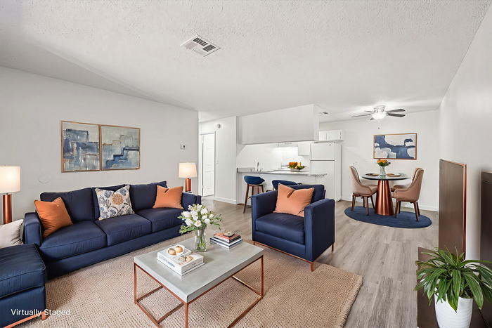 Bright and modern virtually staged living space featuring stylish navy couches, a chic coffee table, and a cozy dining area adjacent to a sleek white kitchen.