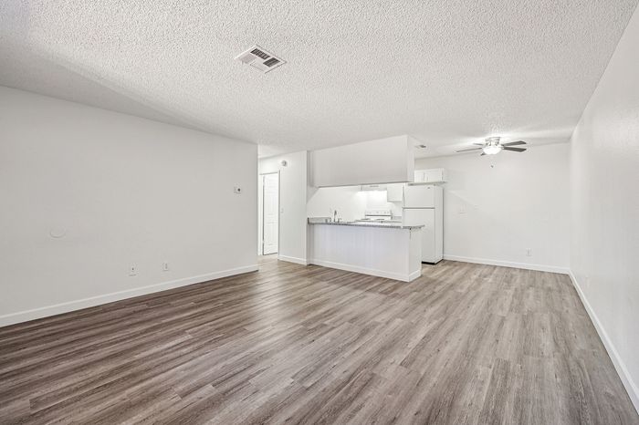Modern open-concept living area with sleek hardwood flooring, a bright white kitchen with appliances, and a ceiling fan for comfort.