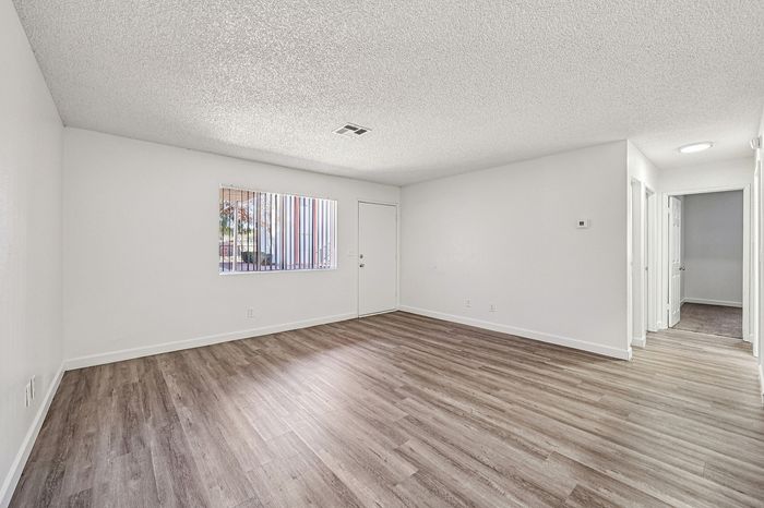 Bright and spacious apartment living area with modern laminate flooring, fresh white walls, and a large window for natural light.