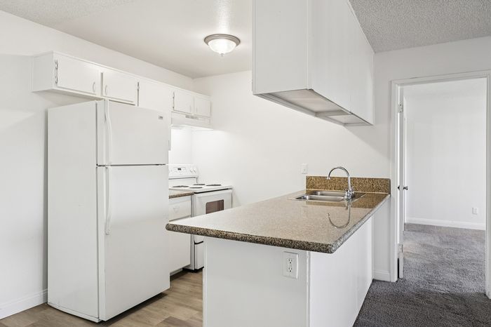 Bright, modern kitchen with sleek granite countertops, white cabinets, and appliances, leading to a cozy carpeted room.