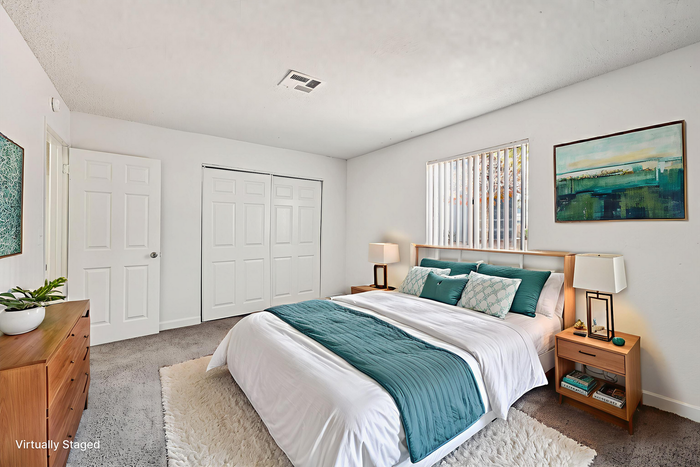 Elegant and inviting bedroom with plush teal and white bedding, warm wood furnishings, modern decor, and ample closet space, showcasing virtual staging at its finest.