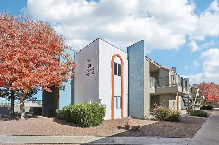 Charming apartment exterior with modern architecture, vibrant autumn foliage, and inviting balcony spaces under a bright blue sky.