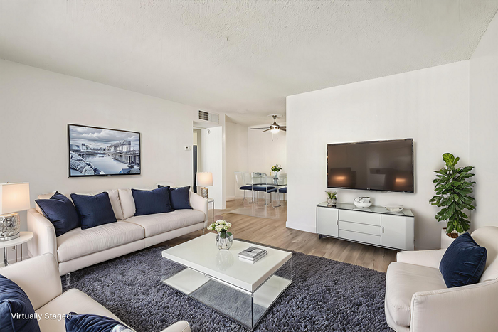 Elegantly staged living room with plush white sofas, navy cushions, and a sleek modern coffee table on a cozy gray rug. Wall-mounted TV and stylish decor create a serene ambiance.