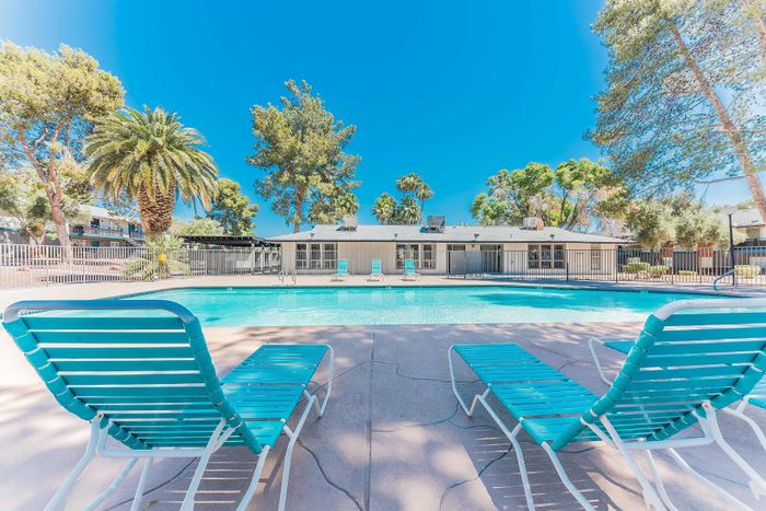 Inviting outdoor pool surrounded by lush palm trees, featuring stylish lounge chairs for relaxation under a clear blue sky.