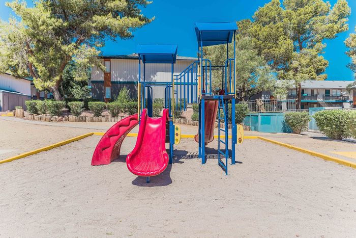 Bright and inviting playground area with a colorful slide and climbing structures, nestled amidst lush greenery and modern apartments.