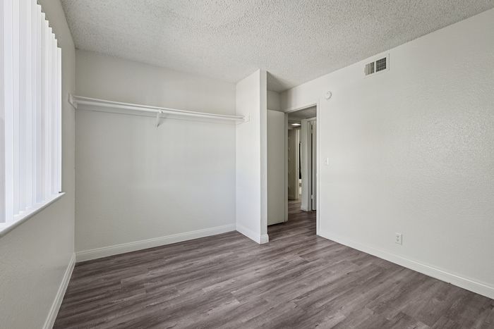 Bright and airy bedroom with sleek wood flooring, large window for natural light, and minimalist design.
