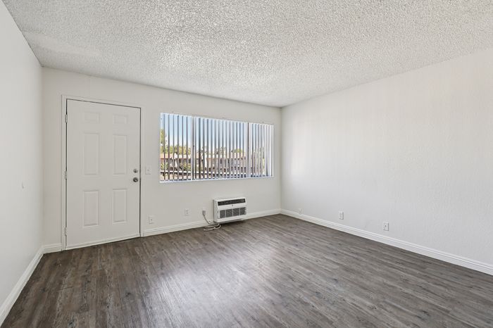 Bright and airy living area with modern laminate flooring, large window with vertical blinds, and sleek white walls.