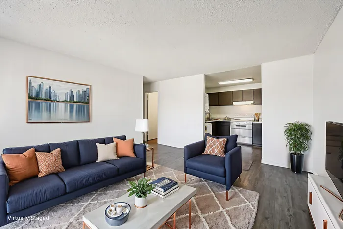 Modern living room with sleek blue seating, accent pillows, and a vibrant wall art, seamlessly connected to a contemporary kitchen. Bright and inviting space accented by a floor plant and stylish decor, ideal for relaxation and entertainment.