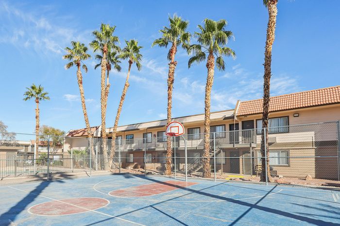 Sunny apartment complex with vibrant palm trees and a welcoming basketball court under a clear blue sky.