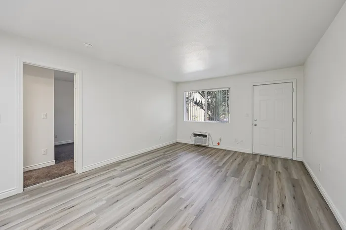 Bright and airy living room with elegant wood flooring, large window, and modern white walls.