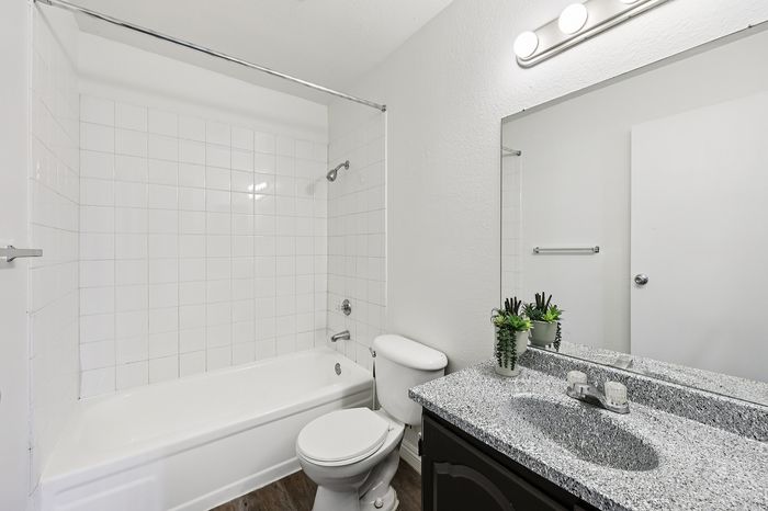 Contemporary bathroom with elegant gray speckled countertop, sleek fixtures, and a cozy bathtub featuring white tiling.