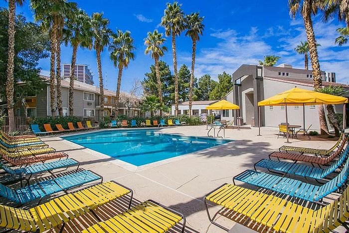 Vibrant outdoor pool area with colorful lounge chairs and yellow umbrellas, surrounded by tall palm trees under a clear blue sky, perfect for relaxation.