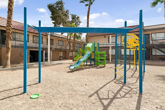 Inviting apartment playground with vibrant blue and green slides, climbing structures, and beautiful palm trees.