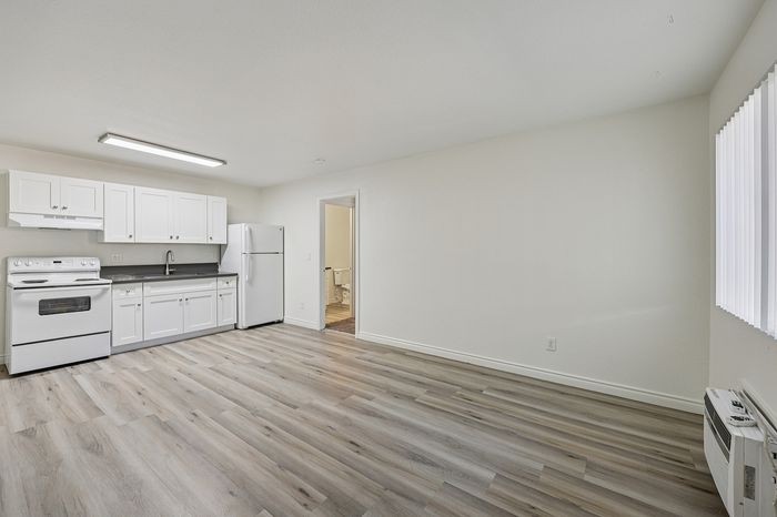 Bright and airy kitchen area with modern white cabinets, sleek countertops, and new appliances, featuring stylish wood flooring and natural light.