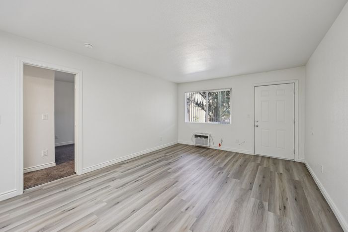 Bright living area with modern wood flooring, large window for natural light, and a doorway leading to additional rooms.