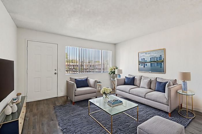 Bright and modern living room with stylish gray couches, elegant decor, and a large window offering abundant natural light.