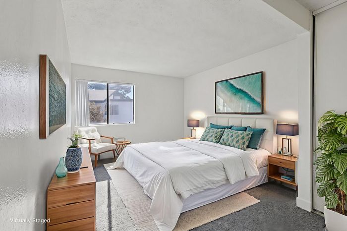Inviting bedroom with stylish decor, featuring a plush white bed, elegant side tables, and vibrant artwork, complemented by natural lighting from a large window.