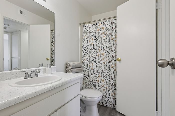Bright and inviting bathroom featuring floral shower curtain, sleek white countertop, and modern fixtures.