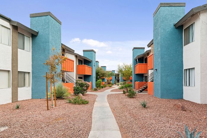 Vibrant apartment community showcasing modern architecture with bold blue and orange facades, complemented by a beautifully landscaped walkway.