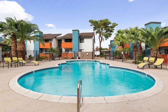 Inviting apartment complex with a sparkling blue pool, surrounded by vibrant palm trees and modern architecture.