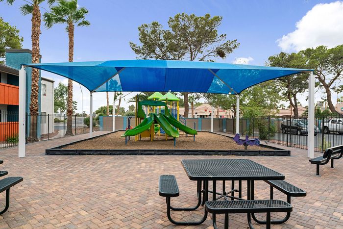 Inviting outdoor playground with vibrant slides under a blue shade, surrounded by lush greenery and seating areas.