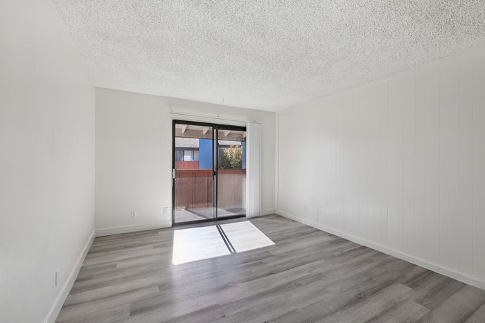 Bright and airy living room featuring sleek hardwood floors and large sliding glass doors opening to a cozy balcony.