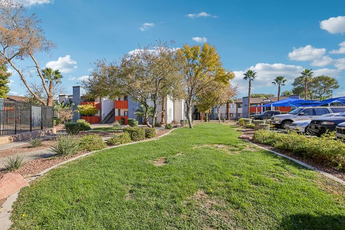 Vibrant apartment complex featuring lush green landscaping, palm trees, and ample parking under a clear blue sky.