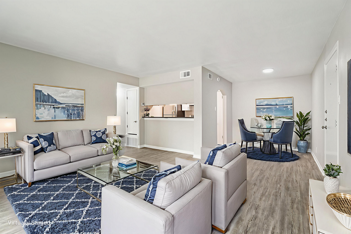 Beautifully staged modern living room with elegant gray sofas, chic blue accents, and a stylish open dining area. Bright and welcoming open-plan layout with sophisticated decor.