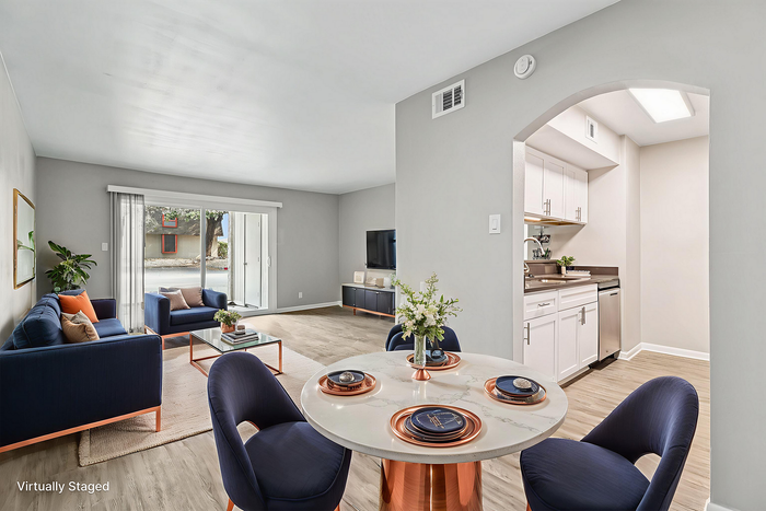 Chic, virtually staged living area with plush navy seating, elegant dining setup, and modern kitchen nook, leading to a bright patio through large glass doors.