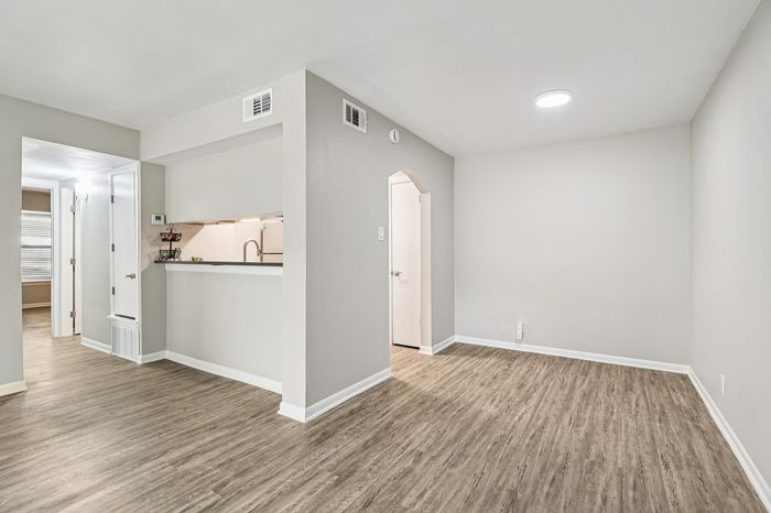 Bright and modern living space with sleek hardwood flooring, archway entrance, and a cozy kitchen nook.