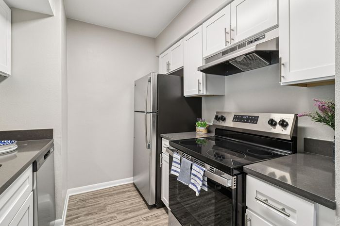 Modern kitchen with sleek stainless steel appliances, elegant white cabinetry, and spacious countertops complemented by wood-look flooring.