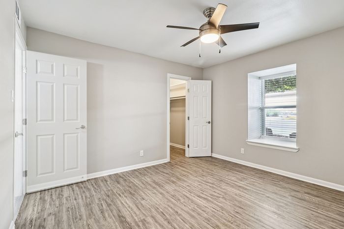 Bright and airy bedroom featuring sleek wood flooring, a modern ceiling fan, and a large window offering natural light.