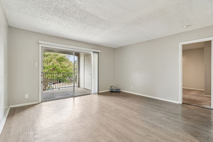 Bright and airy living space with sleek wood flooring and large sliding glass doors opening to a scenic balcony view.