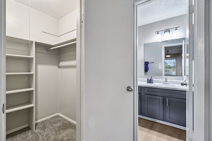 Elegant apartment with a spacious walk-in closet featuring built-in shelving, alongside a modern bathroom with sleek fixtures and ample lighting.