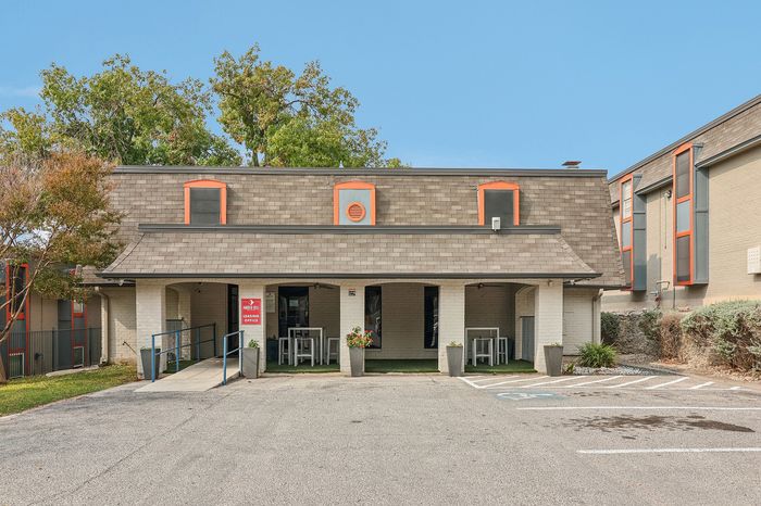 Inviting leasing office exterior with modern design, featuring unique architectural elements, lush greenery, and ample parking space.