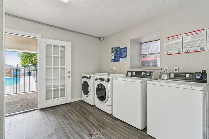 Modern apartment laundry room with sleek washers and dryers, featuring elegant flooring and a view of a sparkling pool through French doors.
