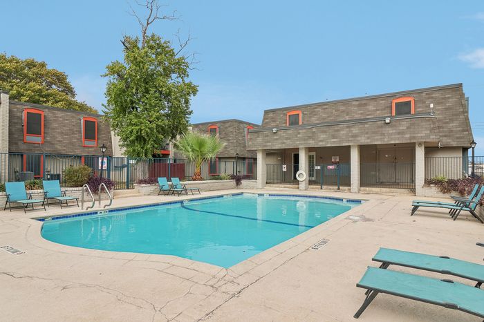 Inviting apartment complex with a refreshing swimming pool surrounded by modern lounge chairs and lush greenery.