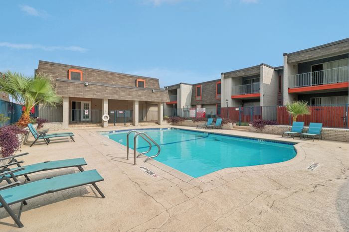 Inviting apartment complex featuring a well-maintained swimming pool area with stylish lounge chairs and vibrant greenery, perfect for relaxation.