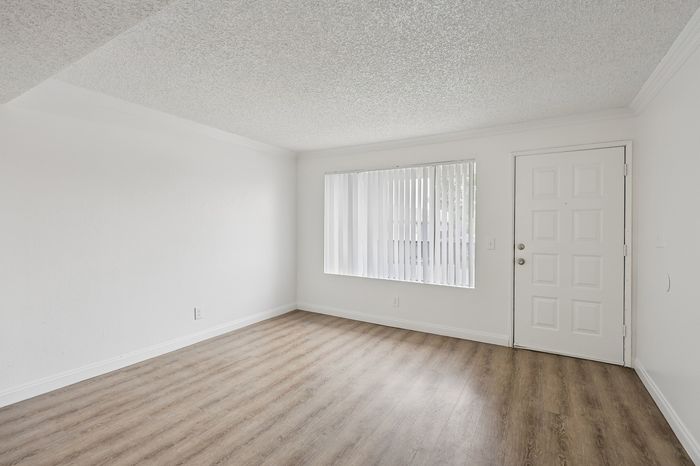 Bright, modern living room with sleek wooden floors and ample natural light through large window.