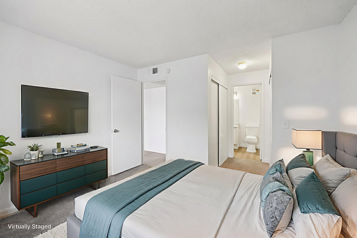 Modern bedroom with chic decor, featuring a mounted TV, stylish dresser, and elegant bed with plush pillows in a bright, airy space.