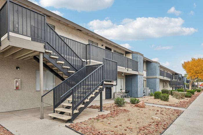 Modern apartment complex with sleek balconies and easy-access stairways, surrounded by well-maintained landscaping under a bright blue sky.