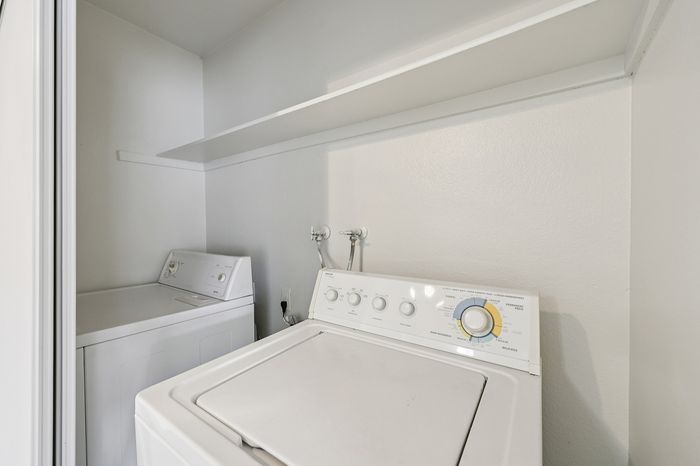 Modern laundry area with energy-efficient washer and dryer set, white interior walls, and convenient shelving.