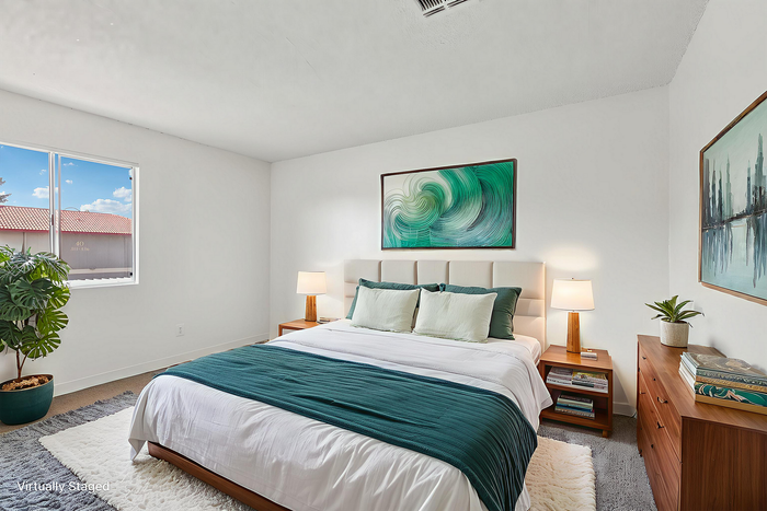 Bright and cozy bedroom with elegant decor, featuring a plush bed with teal accents, stylish artwork, and ample natural light.