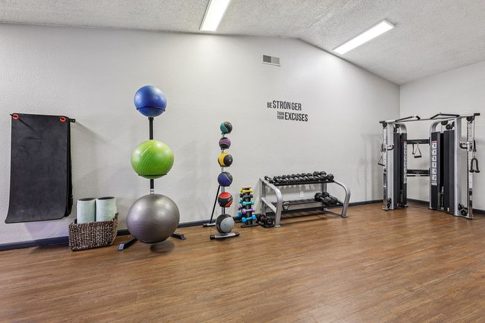 Modern apartment gym with exercise balls, weights, and strength machines on wooden floors. Energizing space with motivational quote.
